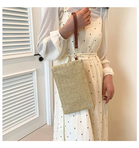 Fashionable straw clutch bag featuring brown leather wrist strap held by a model