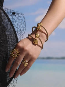Detail of bohemian gold hollow heart bracelet and sun-shaped rings on model hand