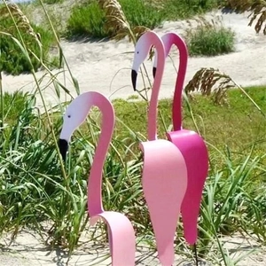 Three pink flamingo garden whirligig stakes placed in an outdoor sandy backyard lawn