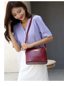 Detailed close-up of a burgundy leather crossbody bag featuring elegant metal hardware accents