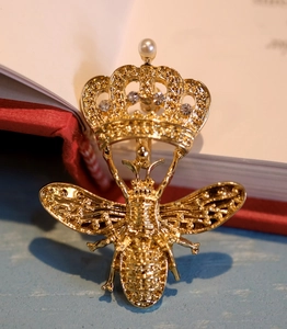 Broche abeille dorée à la mode avec couronne et perle sur un fond de livre classique
