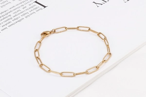 Detailed close-up of a minimalist gold paperclip link bracelet on a white book page