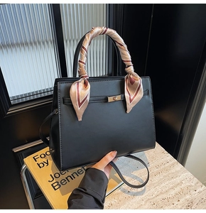 Detailed view of a black textured leather handbag with decorative printed silk scarf and gold lock