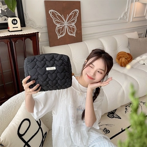 Detail of a black quilted heart pattern cosmetic bag held by a model in a home setting