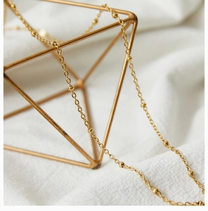 Close-up of golden beaded chain necklace draped over aesthetic geometric metal stands