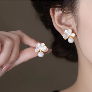 Détail de boucles d'oreilles fleur en nacre avec perle blanche et finition dorée