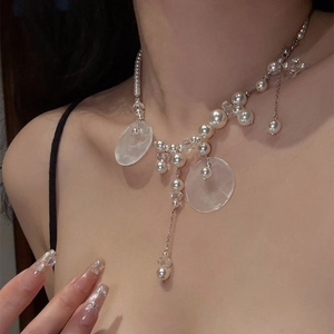 Close-up of pearl necklace with round shell pendant and silver tassels on woman neck