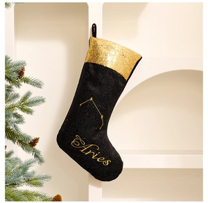 Detail of Aries zodiac Christmas stocking in black and gold hanging on a white shelf