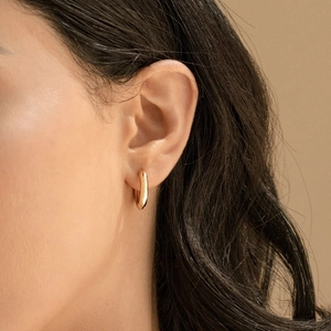 Close-up of a model wearing small minimalist golden hoop earrings with a polished finish