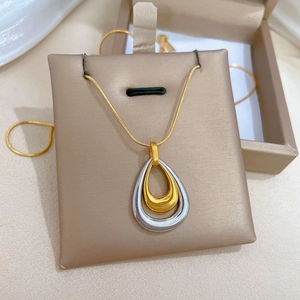 Macro detail of a dual-tone water drop pendant on a gold snake chain necklace