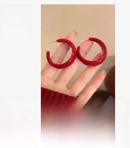 Gros plan de créoles C en acrylique rouge de 3cm montrant la taille et le matériau poli