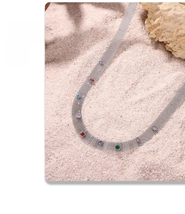 Détail d'un collier en maille tissée avec des zircons colorés sur fond de sable naturel