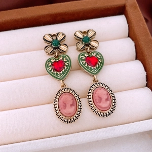 Detail of vintage gold earrings with green clover, red heart, and cameo in a jewelry box