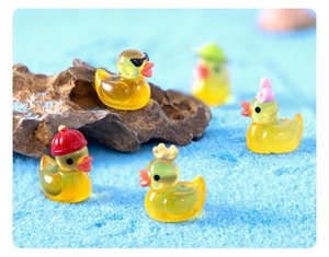 Mini luminous resin ducks with cute accessories on blue decorative sand and rock