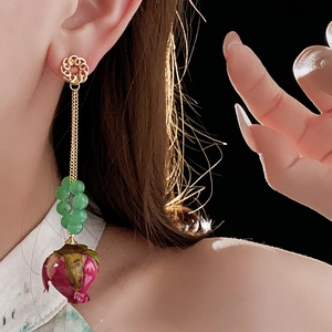 Nahaufnahme langer Vintage-Perlenohrringe mit goldenen Mustern und getrockneten Rosenknospen