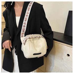 Close-up of a cream white nylon crossbody bag with an ethnic pattern wide fabric strap