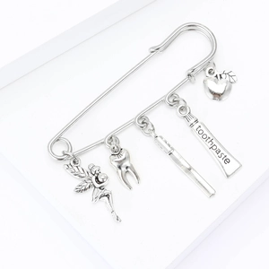 Detailed silver brooch featuring dentist-themed pendants with a fairy and toothpaste