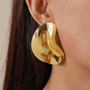 Macro shot of a model wearing large sculptural gold geometric earrings with a polished finish
