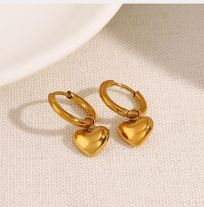 Macro shot of gold heart-shaped hoop earrings on white fabric texture background