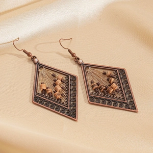 Detailed shot of bronze hollow rhombus earrings with wood beads on golden silk fabric