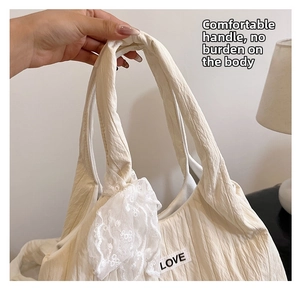 Detailed macro view of cream-colored pleated tote bag featuring lace bow and LOVE label