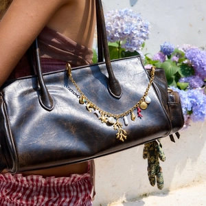 Detail of gold ocean-themed bag charm with shells and seahorse on a brown leather tote