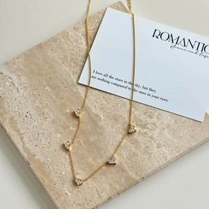 Detailed close-up of a gold necklace with sparkling heart pendants on a stone surface