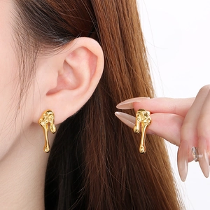 Detailed close-up of gold liquid metal teardrop earrings with a glossy molten finish