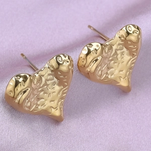 Close-up of golden heart earrings with irregular hammered texture on purple satin fabric