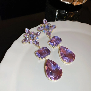 Macro shot of purple floral drop earrings with rhinestones on a white plate