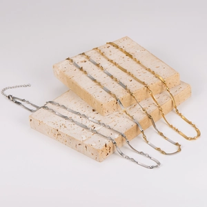 Gold and silver twisted snake chain necklaces displayed on minimalist beige stone props