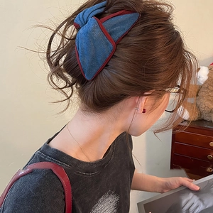 Blue denim bow hair clip with red edges worn on dark brown wavy hair stylish look