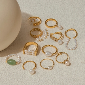 Flat lay of gold titanium steel rings with freshwater pearls and green gemstones
