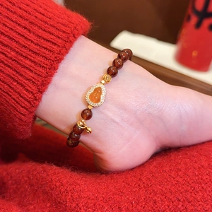 Detailansicht eines roten Achat-Perlenarmbands mit goldenem Kürbisanhänger am Fuß