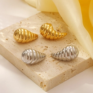 Spiral hollow teardrop earrings in gold and silver finish on a beige stone surface