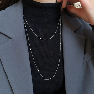 Close-up of layered silver bead necklace worn over a black turtleneck and grey blazer