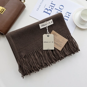 Detail of dark brown cashmere scarf with fringe, brand label, and gift tag set