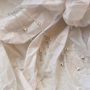 Detailed view of silver heart charms on a delicate link chain over white paper