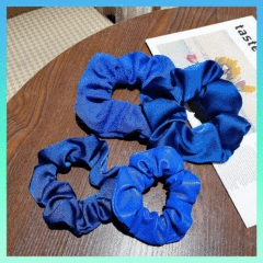 Close-up of three navy blue satin scrunchies in various sizes on a dark wooden desk