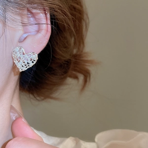 Detail shot of a model wearing silver hollow heart earrings with metallic luster finish