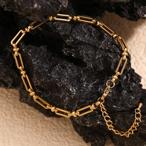 Macro shot of gold paperclip link chain jewelry on black rock with lobster clasp detail