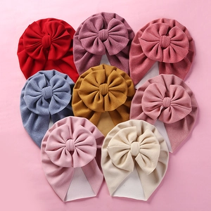 Flat lay of eight colorful cashmere-like baby turbans with large 3D bow decorations