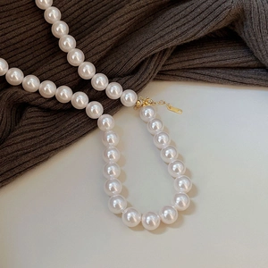 Detail of 10mm white round pearl necklace with gold lobster clasp on knit fabric