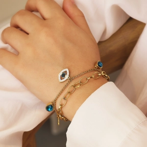 Minimalist evil eye layered bracelet in gold finish with blue pendant on female wrist