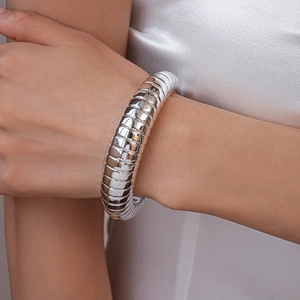 Close-up of a silver chunky segmented bangle on a model wrist against white satin