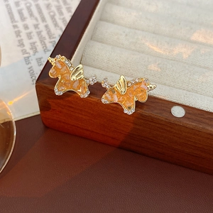 Makroaufnahme von Gold-Einhorn-Ohrringen mit orangefarbenen Steinen auf einer Schmuckbox