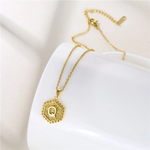 Macro detail of a golden hexagonal pendant with letter Q on a white surface