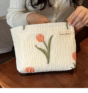 Detail of cream canvas bag with orange tulip embroidery and pleated texture details