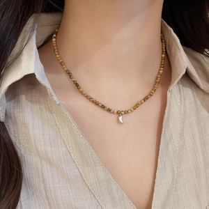 Close-up of a tiger eye beaded necklace with a gold-plated pendant on a model's neck