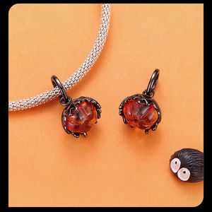 Detail of amber pumpkin charms on a silver bracelet against orange background